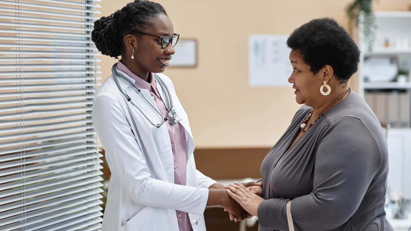 A doctor smiling and holding patient's hands while the patient talks to her.