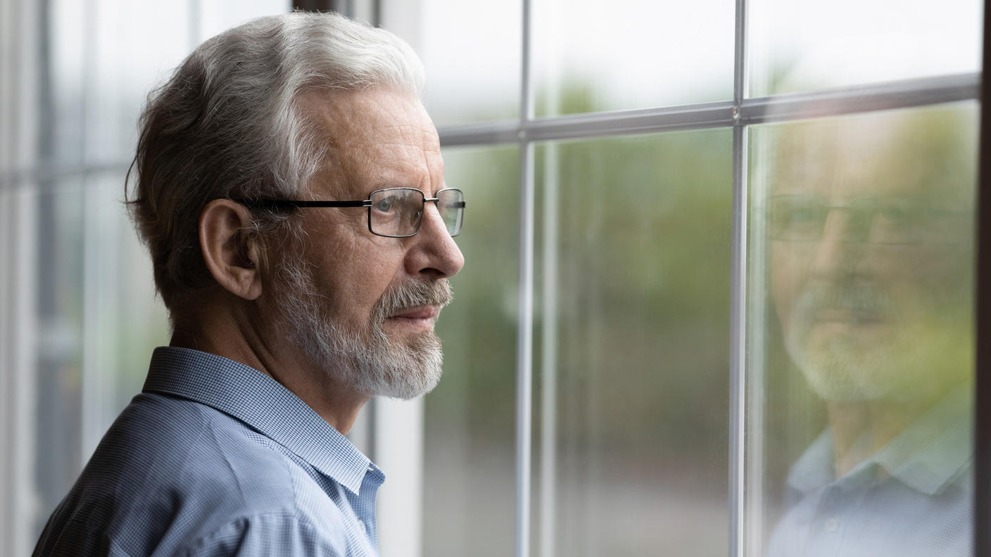 Un hombre mayor con lentes mira por la ventana.