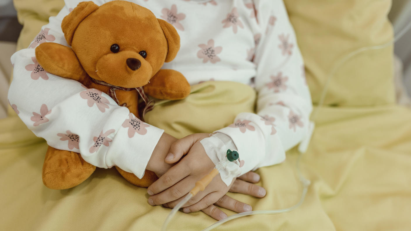 Primer plano de los brazos de una niña que sostiene un oso de peluche mientras recibe una infusión intravenosa