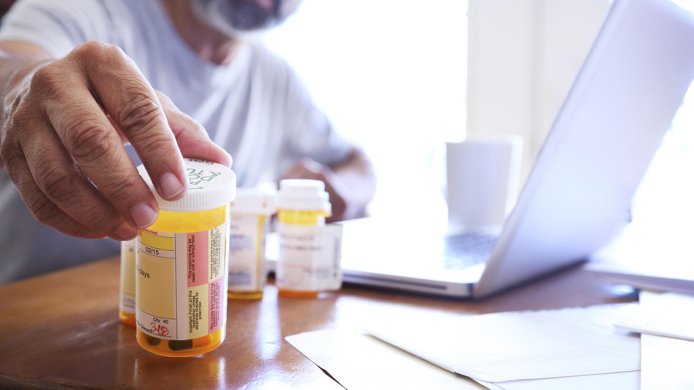 Foto en primer plano de un hombre alcanzando frascos de medicamentos recetados que están sobre una mesa