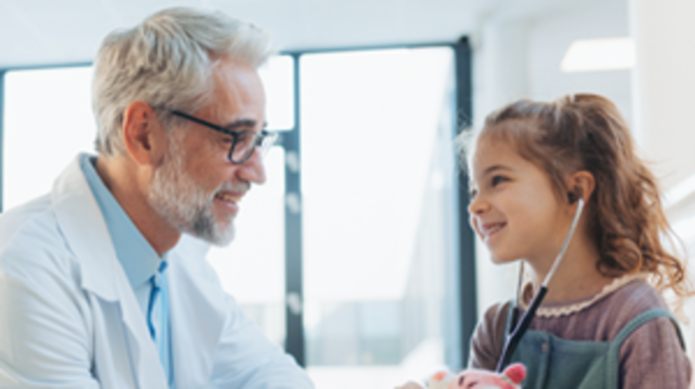 Doctor in white coat with a child patient and stethoscope holding a stuffed animal.