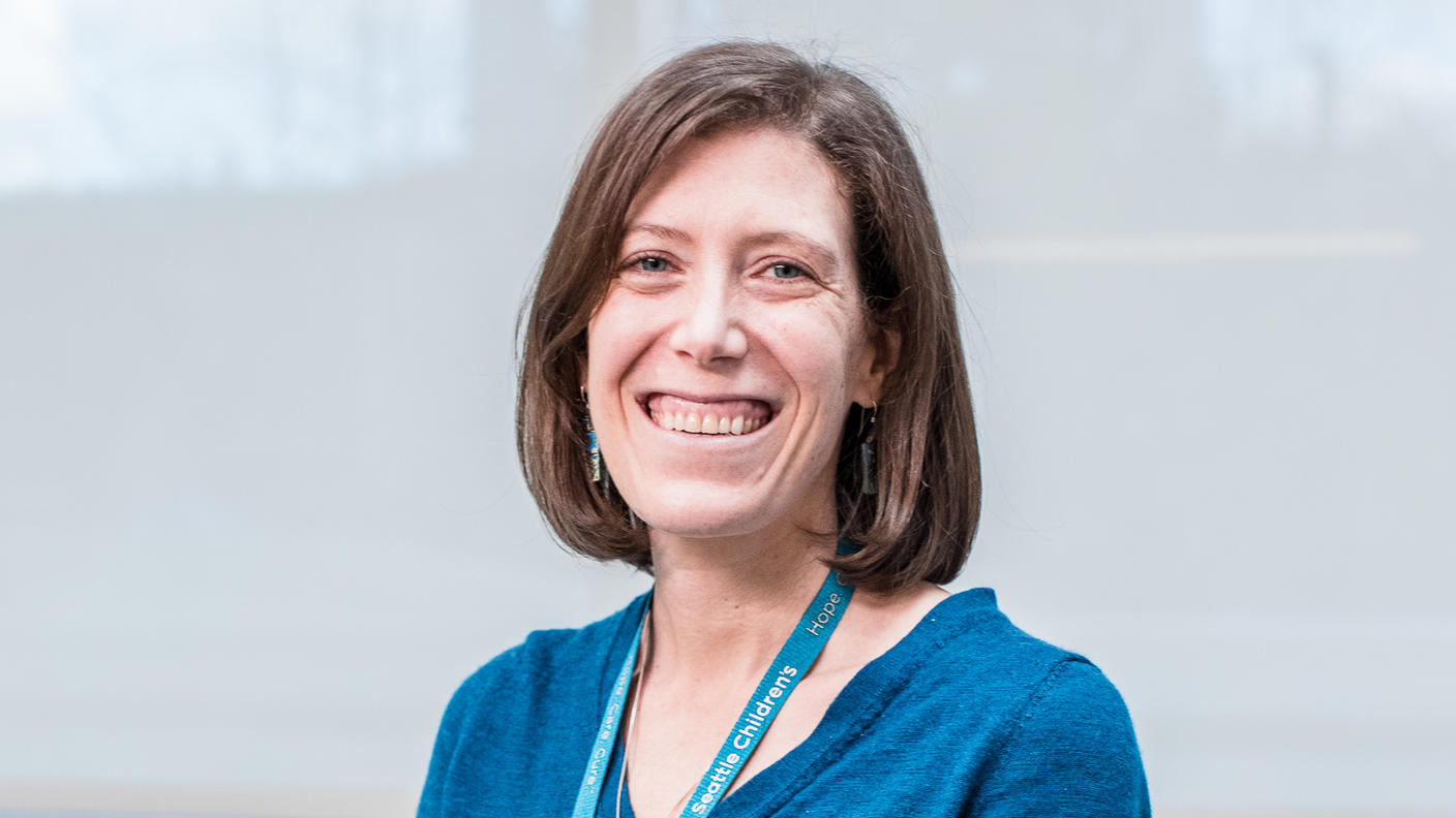 Woman with shoulder length brown hair wearing a blue blouse, necklace, and Seattle Children’s lanyard.
