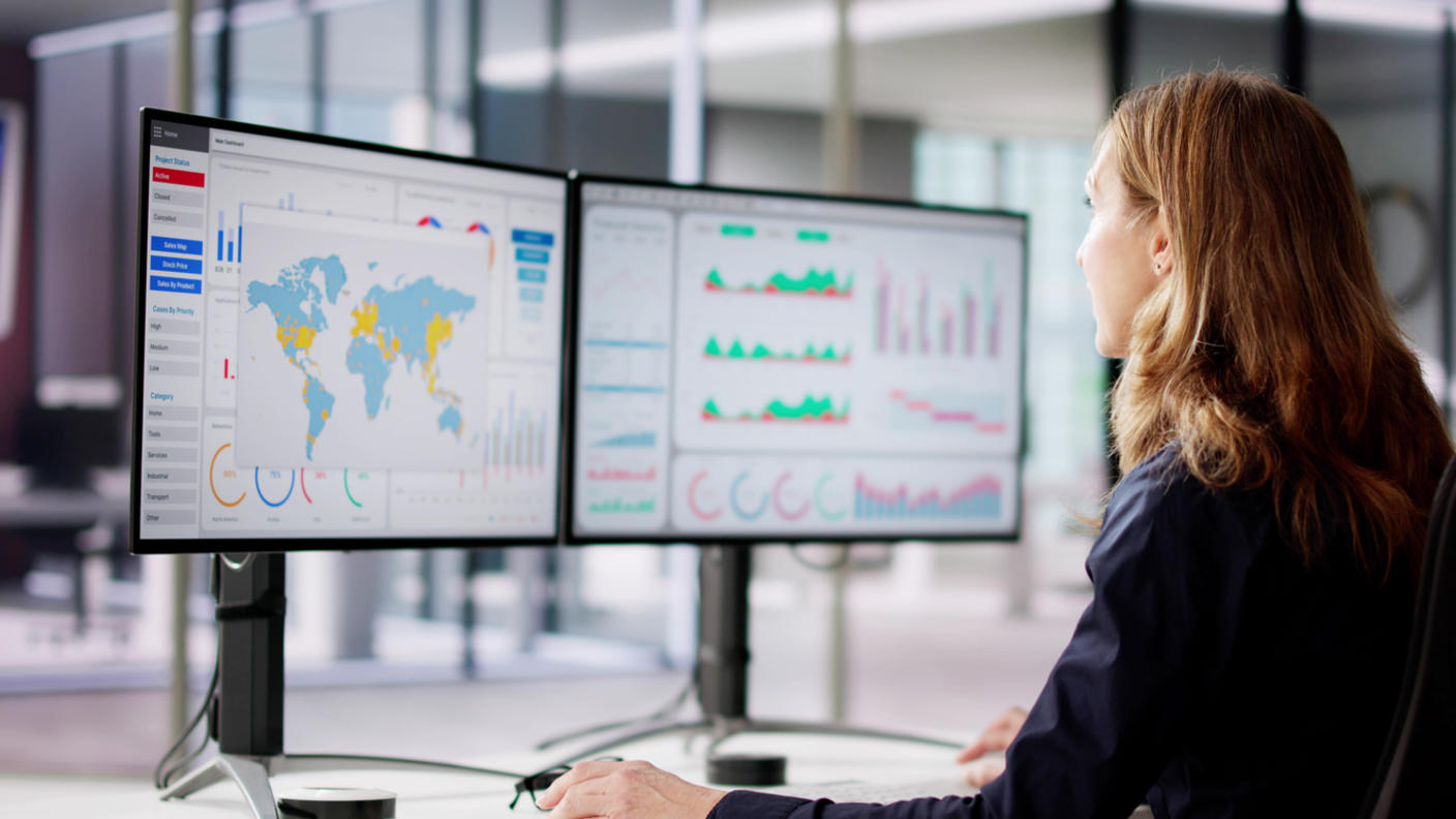 A woman at a desk reviewing data on her desktop screens