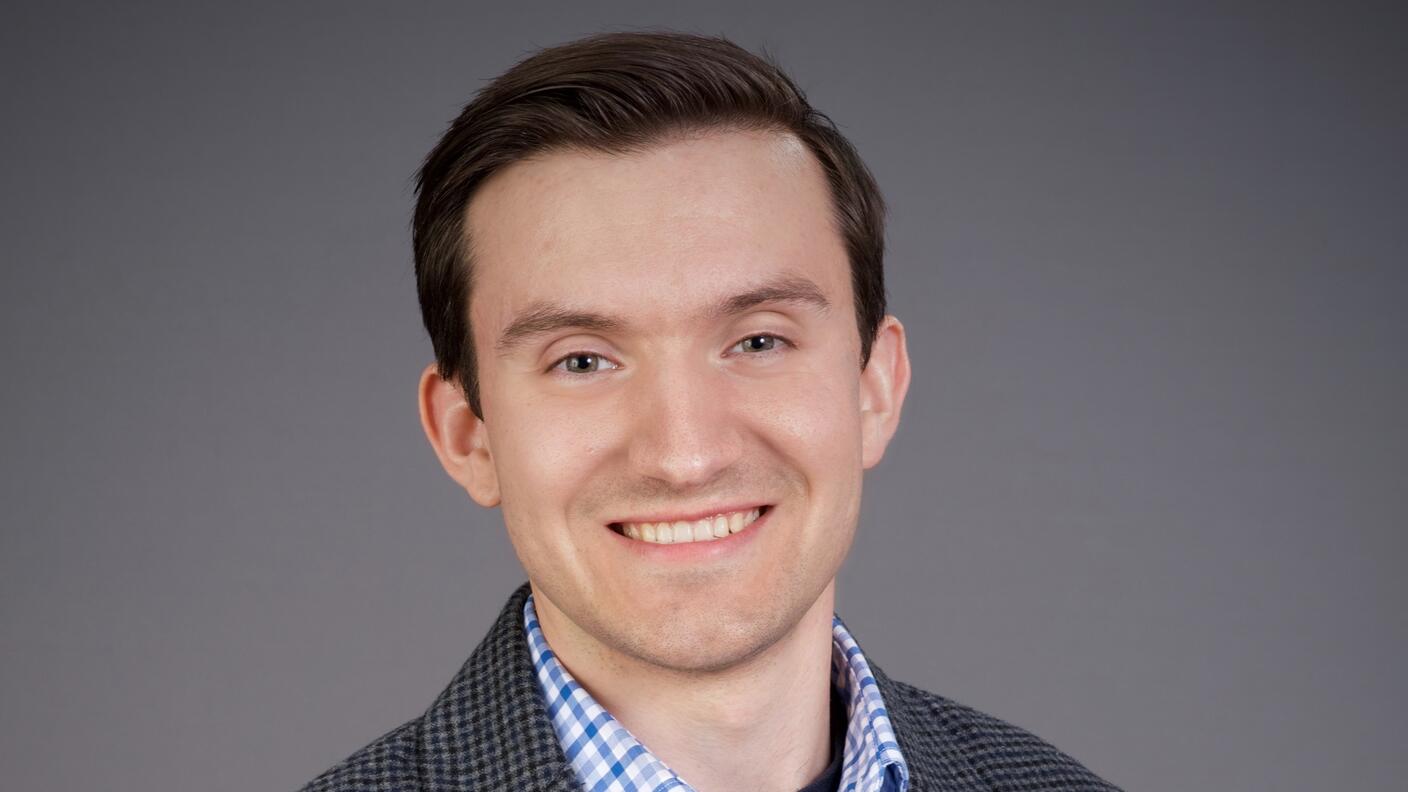 Professional headshot of Dr. Jens Luebeck. He's dressed in a button-down shirt and sports jacket against a gray background.