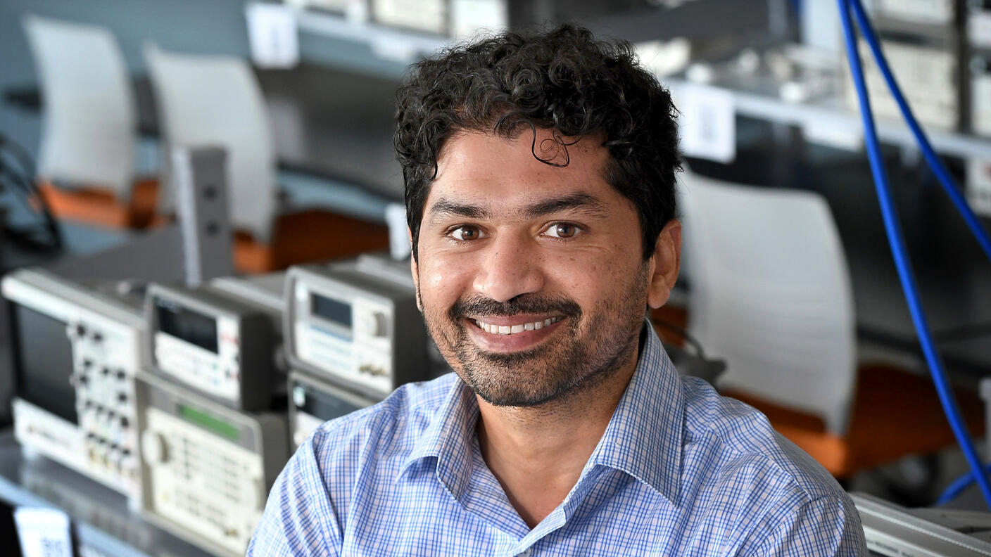Professional headshot of Dr. Ghulam Rasool. He's dressed in a button-down collared shirt against a background of scientific equipment on shelves.