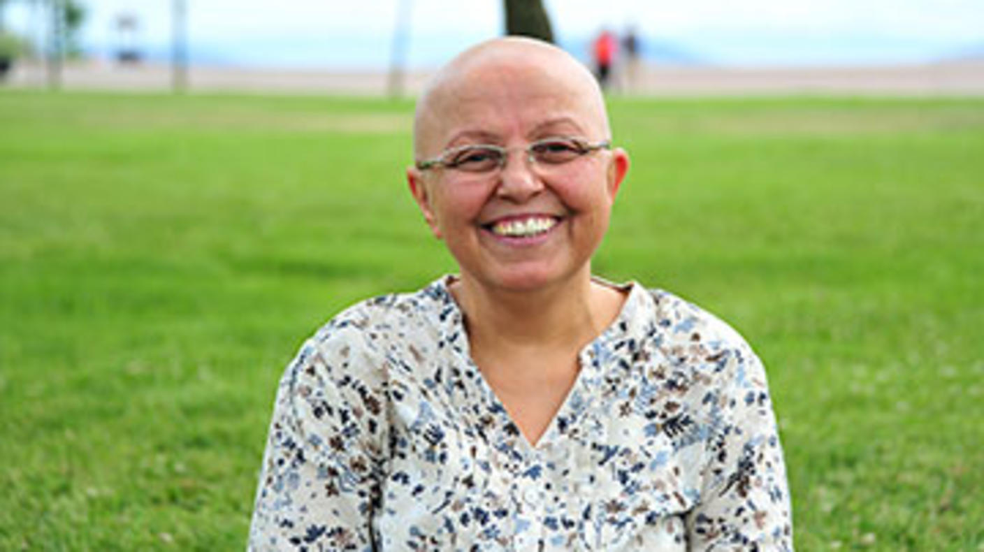Una mujer sin cabello muy sonriente, a sus espaldas se ve un área verde