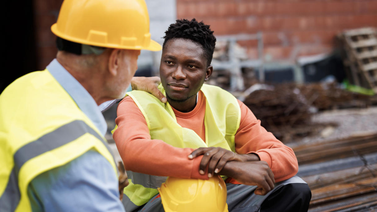 Construction worker sitting down with coworker’s hand on his shoulder.
