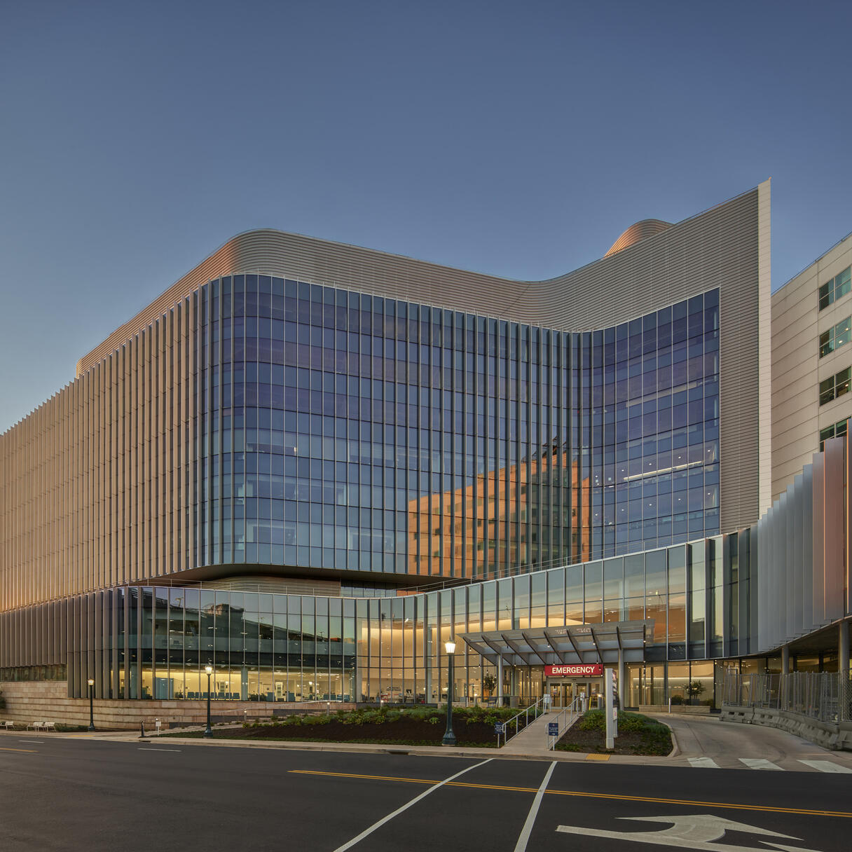 Exterior of a hospital with many reflective windows shot during the sunset. There’s a red entrance sign with white letters that says “Emergency”.