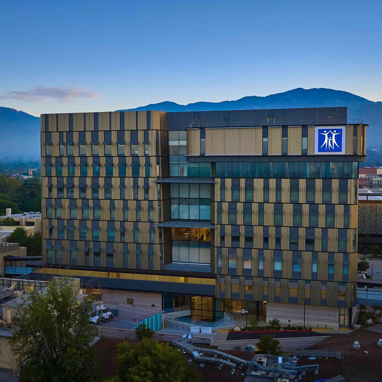 City of Hope Comprehensive Cancer Center building with patterned facade, set against mountains at dusk.