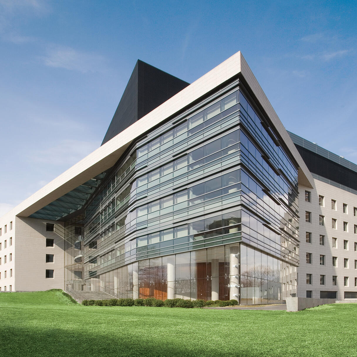 Modern glass-and-stone Albert Einstein College of Medicine building with sharp angular rooflines and a large lawn in front under a clear sky.