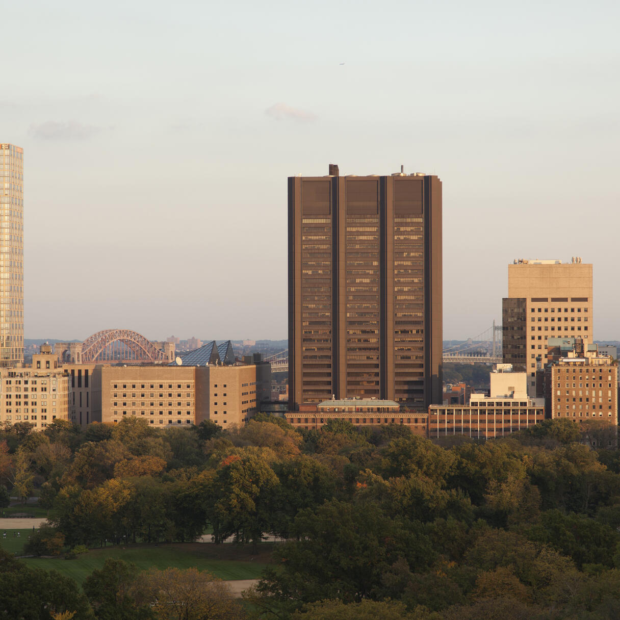 The Tisch Cancer Institute at Mount Sinai near a large park with city buildings and distant bridges at sunset.