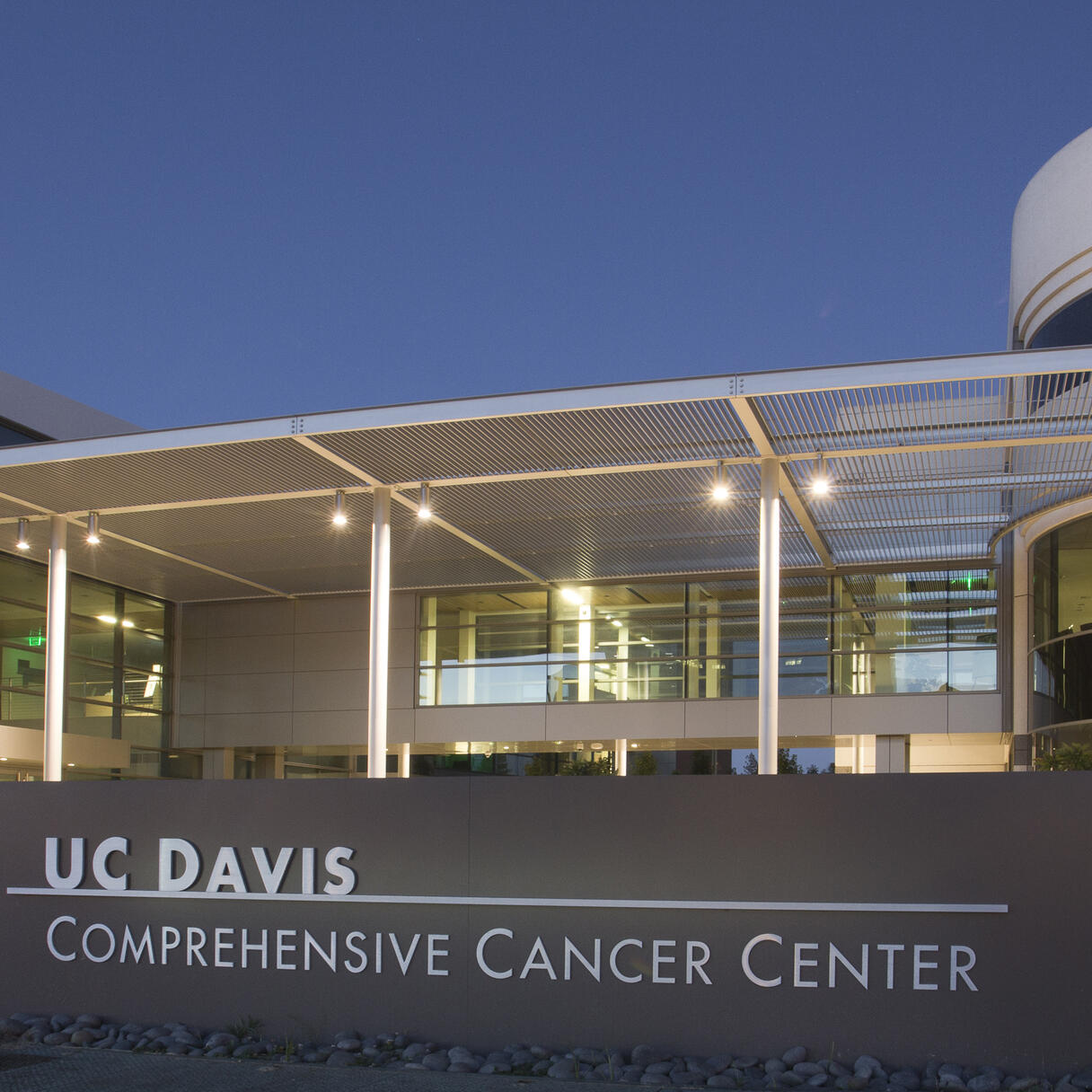 UC Davis Comprehensive Cancer Center entrance with illuminated sign and modern glass buildings at dusk.