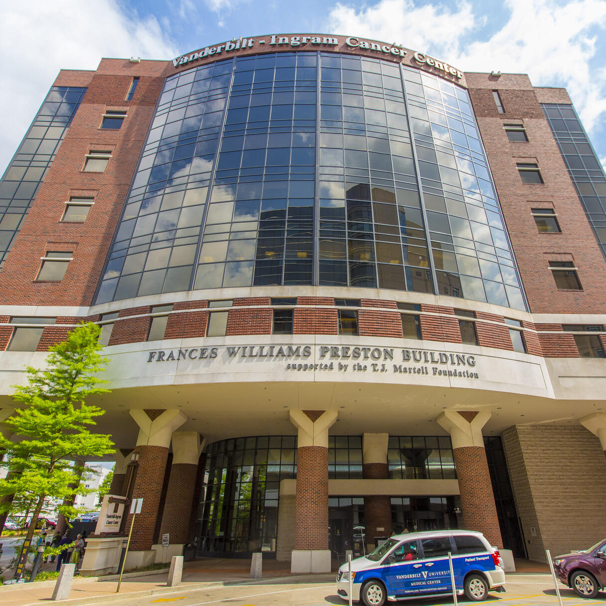 Vanderbilt-Ingram Cancer Center building with a curved glass facade and brick exterior, viewed from street level under a partly cloudy sky.
