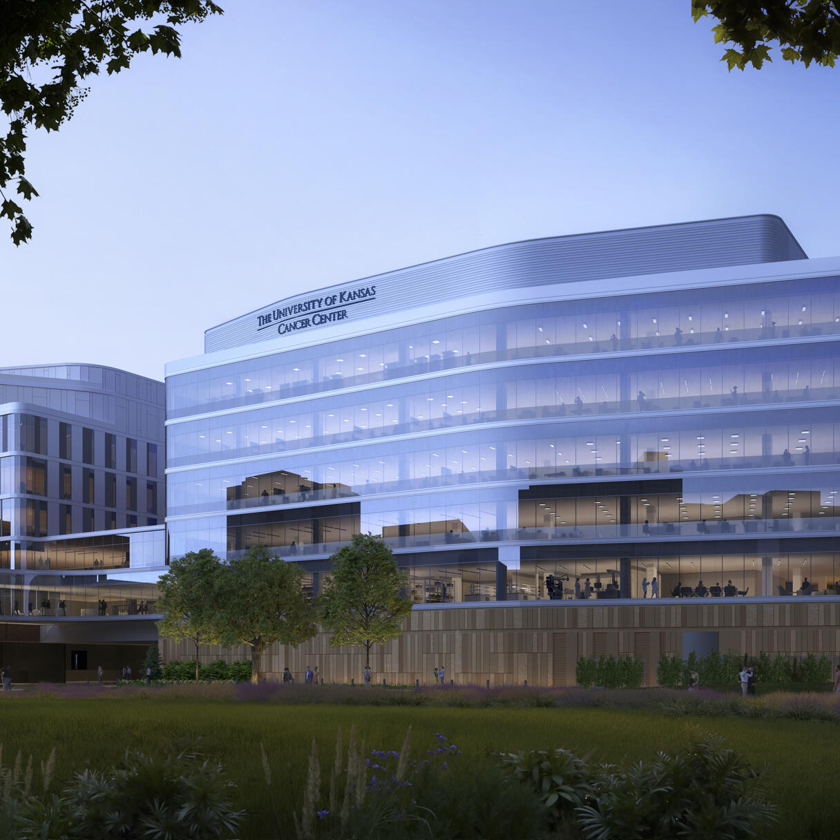 University of Kansas Cancer Center, a large modern glass building surrounded by trees, landscaped grounds, and walkways at dusk.