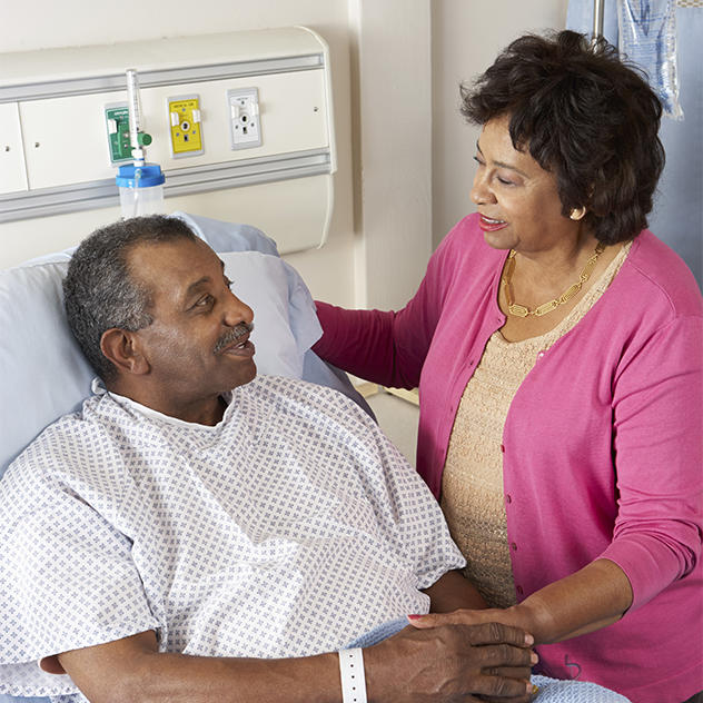 Woman visits male patient who is sitting up in a hospital bed.