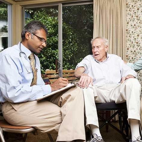 Male health care provider meets with senior male patient and a female caregiver at home.