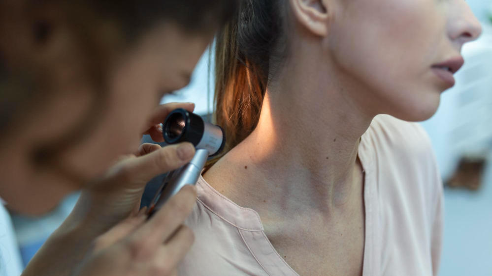 Doctor examines mole at base of person's neck.